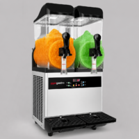 Dual-hopper slush machine dispensing orange and green slush with black lids and silver body, glossy controls, and a dual drip tray below