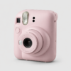 Pink instant camera close-up facing front, showing the lens, flash, and viewfinder on a light background.",