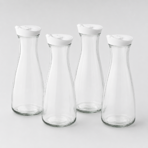 Four tall, clear glass bottles with white caps arranged together against a light gray background.