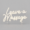 Neon sign that reads 'Leave a Message' in cursive, mounted on a gray backdrop with clear stands nearby (decorative display).