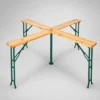 Outdoor wooden picnic table with four benches arranged in an X shape around a central supporting post with green metal legs.